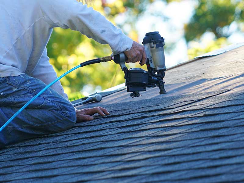 Close up of a worker installing new gray shingles on a residential roof with a nail gun